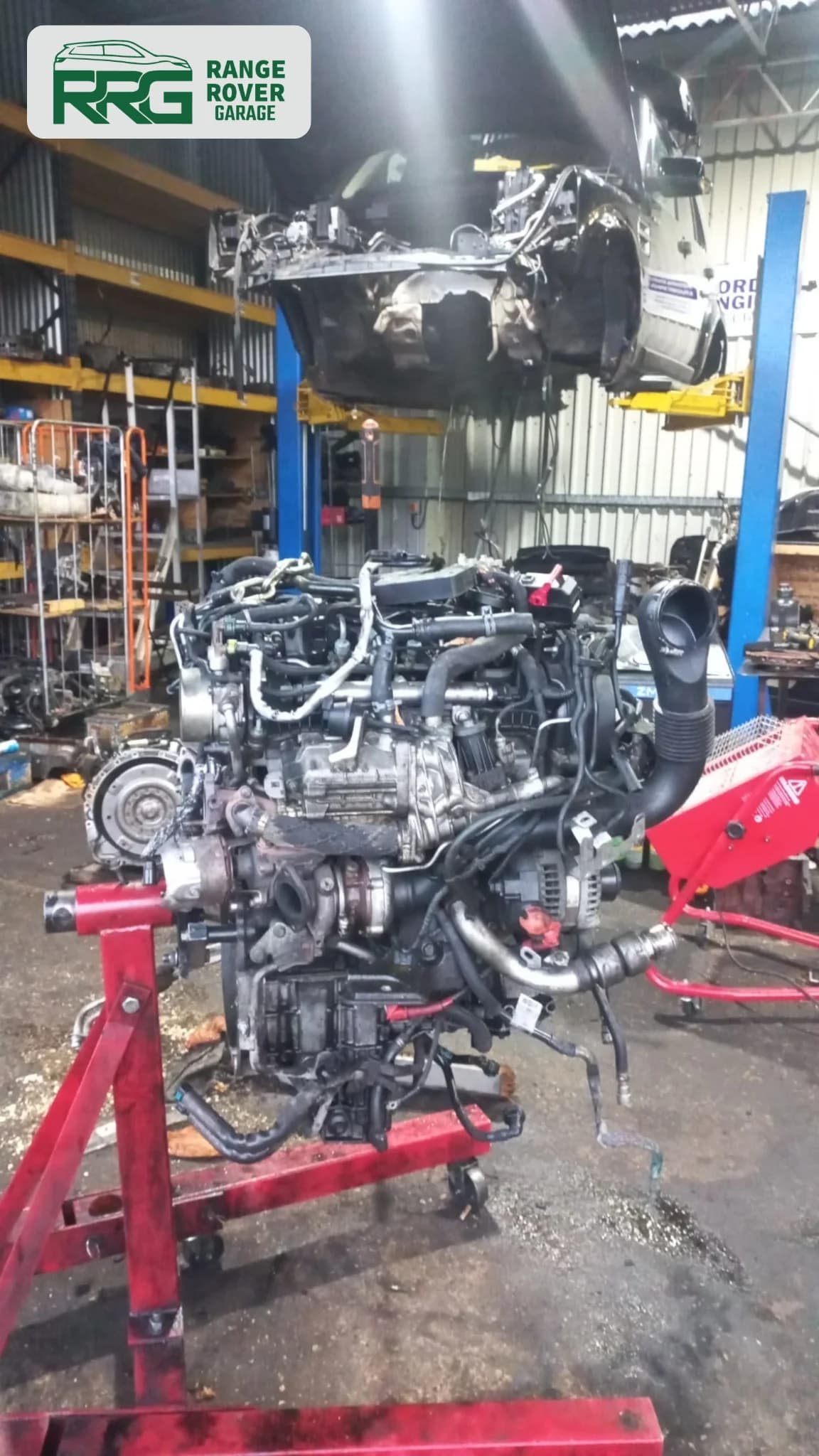 Removed engine supported on a red stand beside a workshop lift