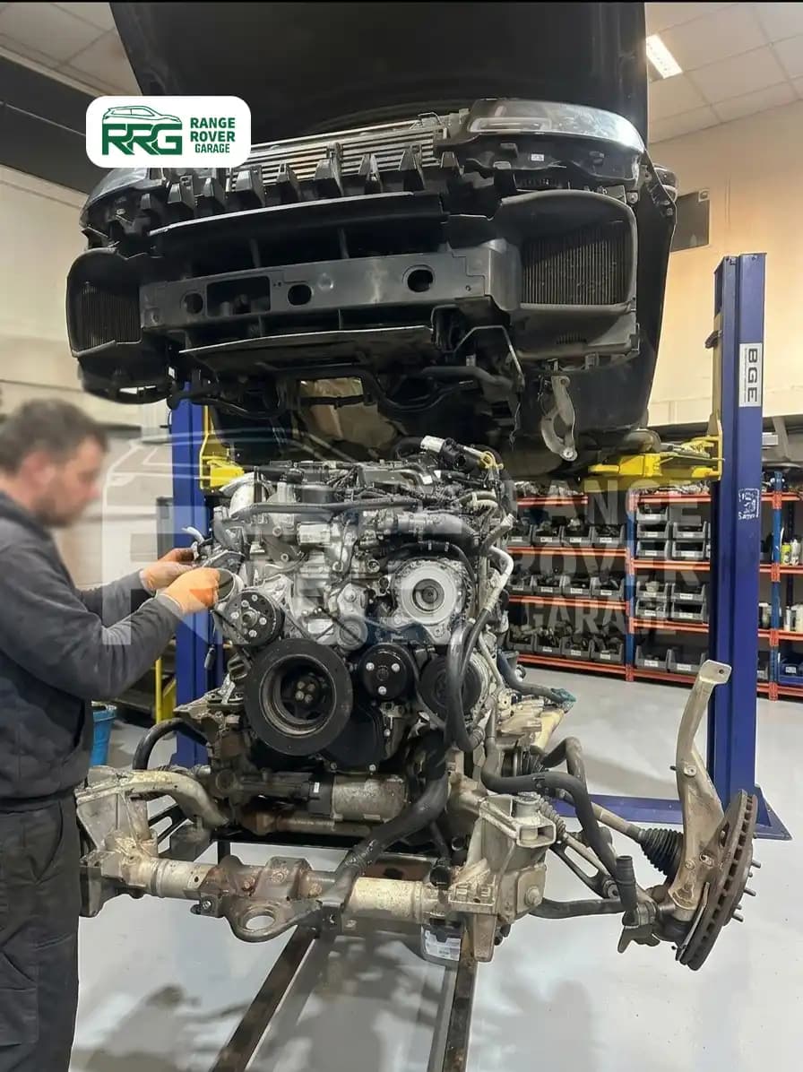 Mechanic working beside a removed engine below a raised Range Rover