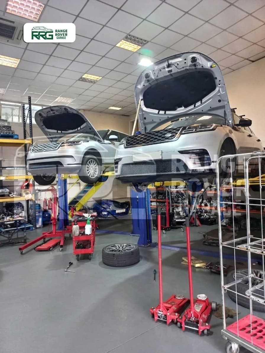 White Range Rover on a lift beside engine hoists and workshop tools